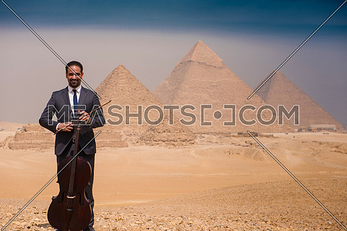 chello player in egyptian desert with pyramids in background