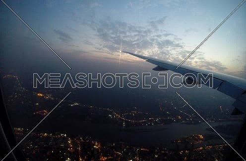 shot from plane window showing wing while flying over a city   at sunset