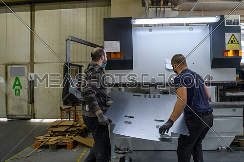 two workers wearing a protective mask due to a coronavirus pandemic, working in a modern factory, and preparing a program and materials for a CNC machine. High quality photo