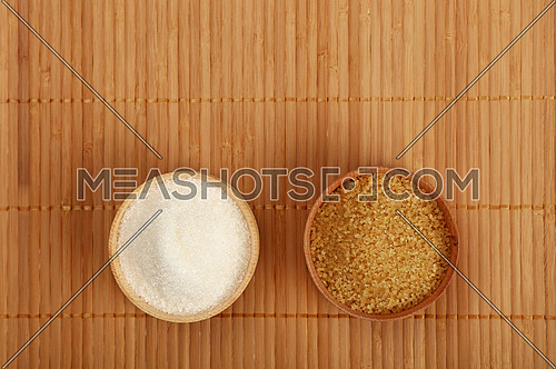 Choice, selection of two sugars in small wooden bowls on bamboo mat background, brown cane and white sugar, top view