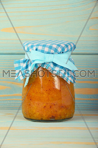 One glass jar of homemade quince jam with textile top decoration at blue painted vintage wooden surface