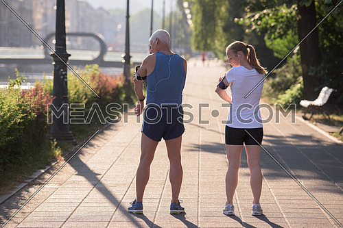 jogging couple check music playlist on phone and plan route before morning running workout  with sunrise in the city  and sun flare in background