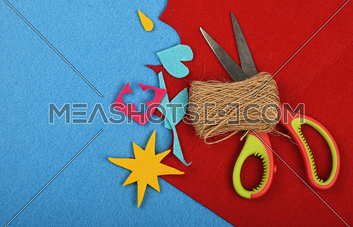 Craft and art, felt pieces, cuts, jute twine thread bobbin and scissors on red and blue background