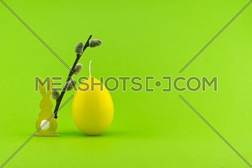 Minimalistic Easter holiday or spring background with Easter Hare figure, pussy willow branch and egg shaped candle over a green background. Copy space for your text