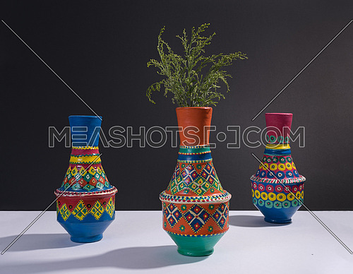 Studio shot of still life of three orange ornate pottery vases with two yellow and violet flower in a background of black table and white wall
