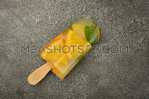 Close up several fruit ice cream popsicle with fresh orange slices, green mint leaves and ice cubes on gray table surface, elevated top view, directly above