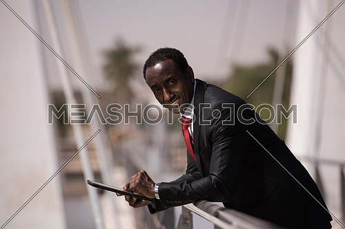 portrait of young african american businessman on bridge while working on tablet computer