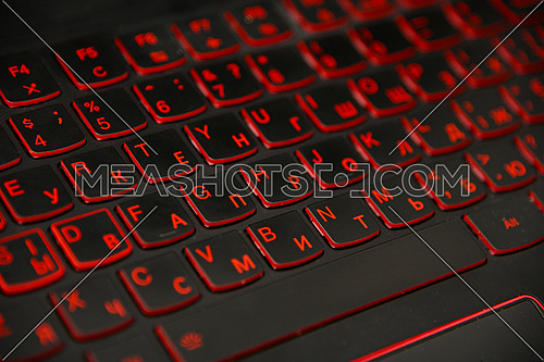 Close up red led backlit computer laptop keyboard keypad with dual alphabet, English and Cyrillic, high angle view