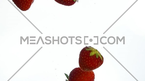 Close up several fresh red ripe strawberries thrown and floating in clear transparent water, low angle side view, slow motion