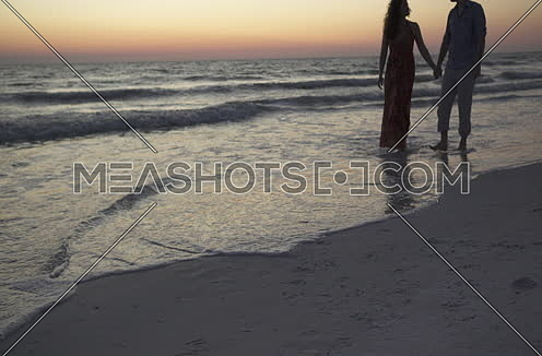 A couple holding hands and walking by the beach during sunset