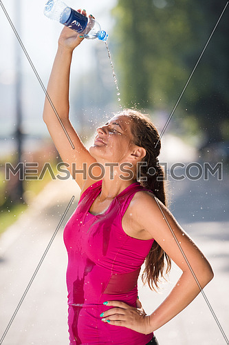 Athlete woman runner pouring water from bottle on her head after jogging in the city on a sunny day