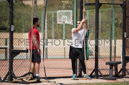 wo young middle eastern athletic built men strenuous exercise climbing the rope outside on a sunny day