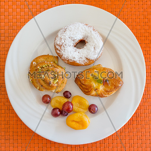 In the pictured three pastries served on a white plate with fruits as decoration.