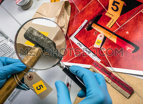 Expert police examines with magnifying glass a hammer in laboratory forensic equipment, conceptual image