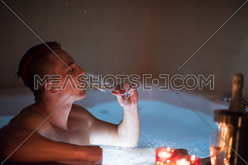 young handsome man enjoys relaxing in the jacuzzi with candles and champagne at luxury resort spa