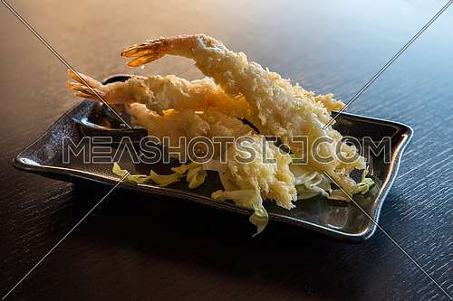 Japanese Cuisine - Tempura Shrimps (Deep Fried Shrimps) with sauce and vegetables on a black plate.