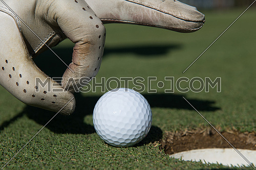 close up of man's hand putting golf ball in hole at course