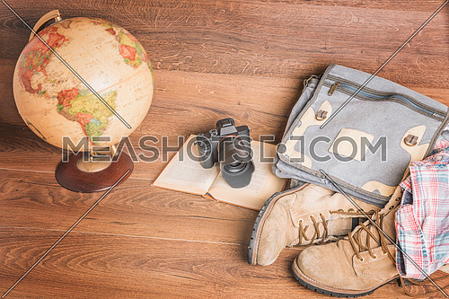 Front view of globe,camera,book,bag,boots and shirt, wooden background,vintage look for travel concept.