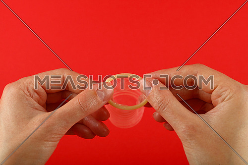 Close up two woman hands holding one open latex condom over red background with copy space, low angle side view