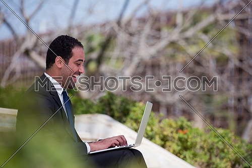 Handsome business executive sitting on stairs if a corporate building working on laptop