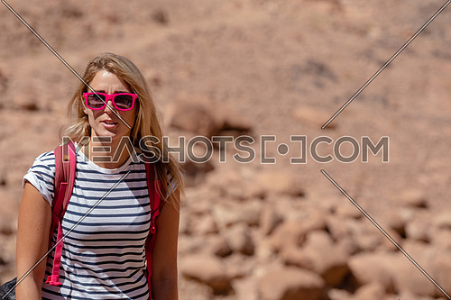 Long shot for a female tourist wearing a pink glasses and travel backpack taking exploring at Sinai Mountain for wadi Freij at day.