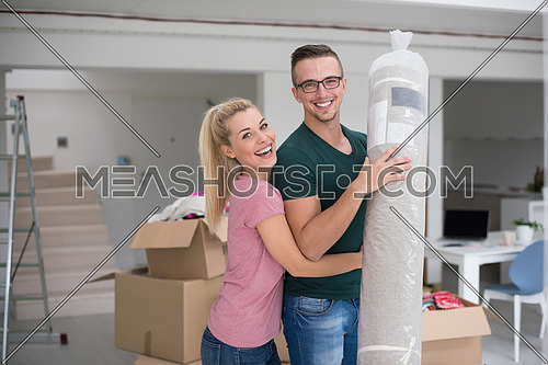 Young couple carrying a carpet moving in to new home together. Home, people, moving and real estate concept