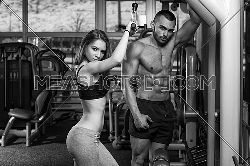 Strong Young Couple Working Out On Machine For Triceps In The Gym With Exercise Equipment