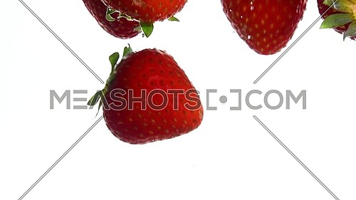 Close up several fresh red ripe strawberries thrown and floating in clear transparent water, low angle side view, slow motion