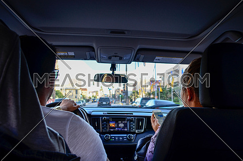 Two people in the front seats of a car, the husband driving and wife is checking her sell phone while listing to some music