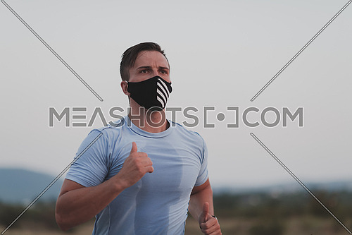 Fitness man in wet sporty clothes wearing black protective face mask running outdoors in the city during coronavirus outbreak. Covid 19 and physical jogging activity, sport and fitness. New normal
