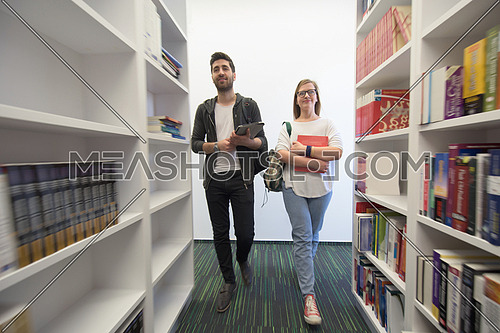 happy students group  in school  library selecting books to read and walking