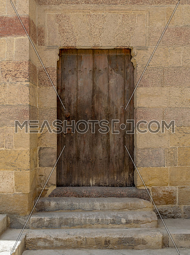 Grunge wooden aged door on exterior stone bricks wall of Amir Aqsunqur Mosque (Blue Mosque), Medieval Cairo, Egypt