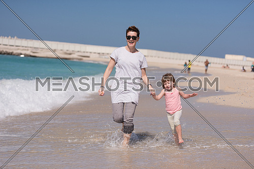 beautiful young mother and cute little girl are enjoying while running on exotic beach along the ocean Travel and Vacations.