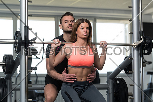 Personal Trainer Showing Young Woman How To Train Barbell Squats Exercise In A Gym