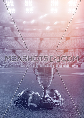 closeup shot of american football,helmets and trophy on grass field at modern stadium with flares and lights at night