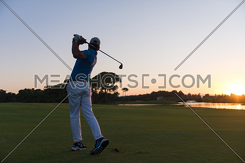 golfer hitting long shot with driver on course at beautiful sunset