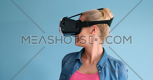 Happy girl getting experience using VR headset glasses of virtual reality, isolated on blue background