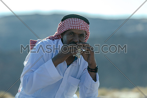 Portirat for a bediuon male wearing traditional clothing and eating in Sinai at day.