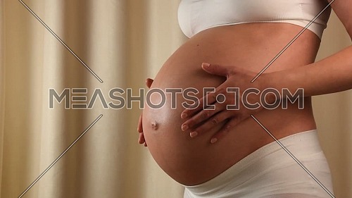 Close up profile view of pregnant Caucasian woman holding and touching her exposed belly with hands anticipating baby birth