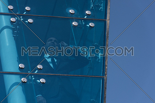Outdoor shoot showing a young business executive talking over the phone through glass front of a corporate building with blue sky in background