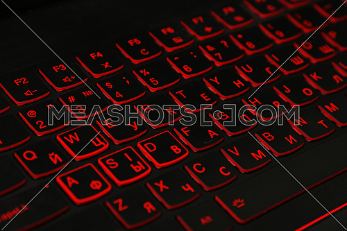 Close up red led backlit computer laptop keyboard keypad with dual alphabet, English and Cyrillic, high angle view