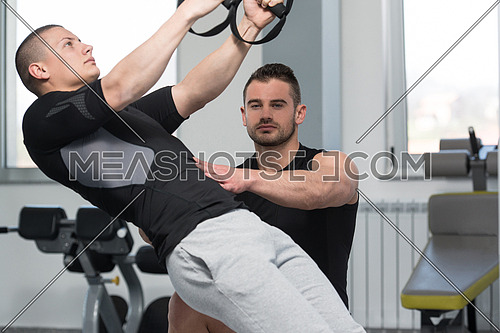 Personal Trainer Showing Young Man How To Train With Trx Fitness Straps In A Health And Fitness Concept