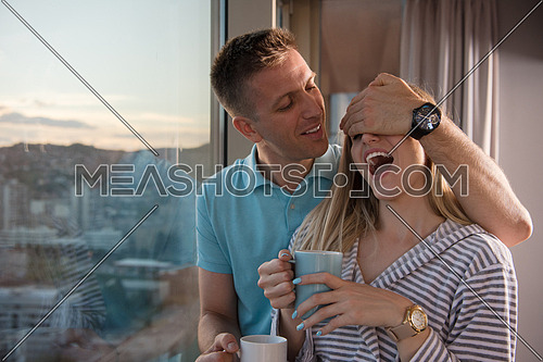 romantic happy young couple enjoying evening coffee and beautiful sunset landscape of the city while standing by the window