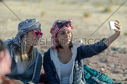 mid shot for two female tourists wearing bedouin traditions headscarf and taking selfies at Ain hodouda in Sinai at day