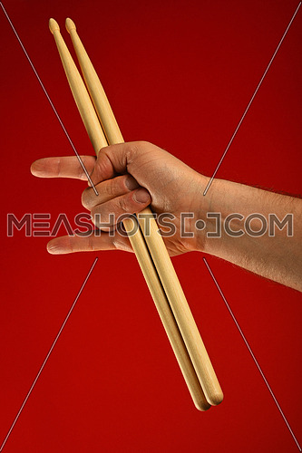 Man hand holding two drumsticks with devil horns rock metal gesture sign over red background
