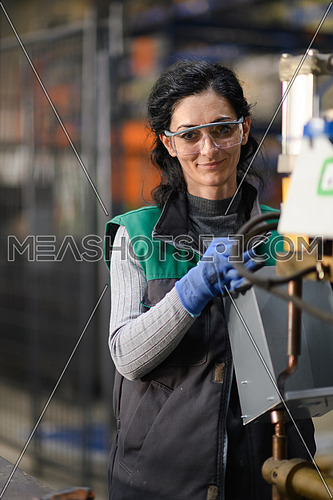 Woman worker wearing safety goggles control lathe machines to drill components. Metal lathe industrial manufacturing factory. High quality photo