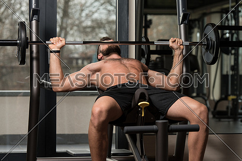 Handsome Man Is Working Out Chest With Barbell In A Modern Gym