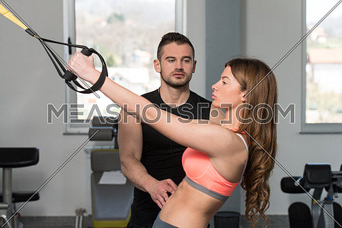 Personal Trainer Showing Young Woman How To Train With Trx Fitness Straps In A Gym