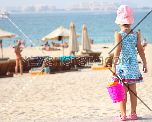 Girl at the beach holding bucket and toys