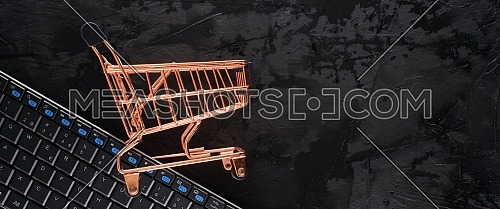 Golden shopping cart on black grunge background with copy space for text in a panoramic format to use as header or web banner. Black Friday sale, shopping concept